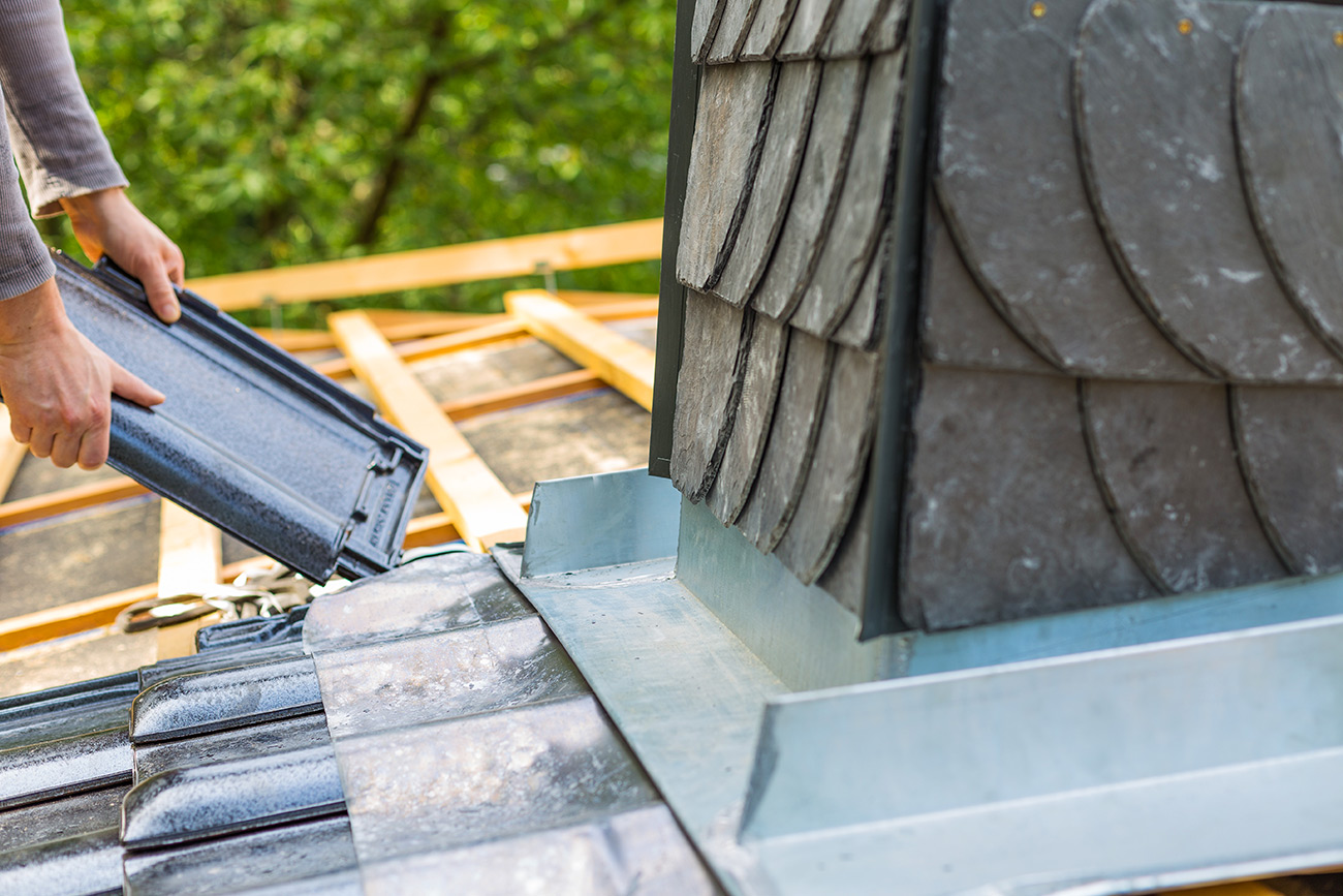 Dachdecker in Stuttgart legt eine Dachziegelplatte auf ein Dach mit Schieferverkleidung und Metallabdeckung